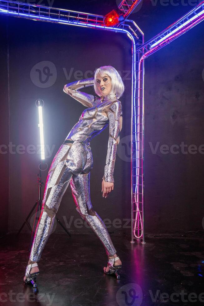 Blonde as cyber robot. Girl in shining silver armor in neon. Blonde with fantastic makeup and image in dark key and colored light, posing in cyberspace. She stands in a glowing cube photo
