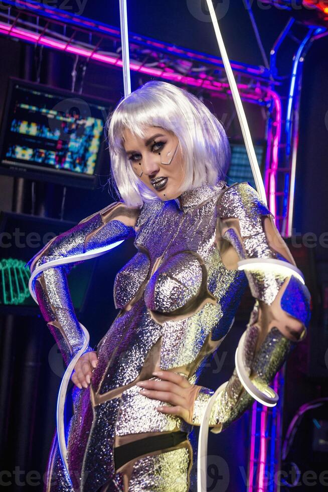 Blonde as a cyber robot. Girl in shining silver armor in neon. Blonde with fantastic makeup and image in dark key and colored light, posing in cyberspace. her hands are wrapped with a wire that glows photo