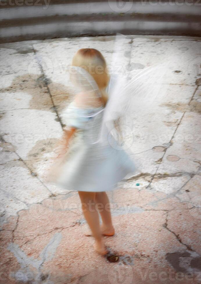 cute blonde girl in fairy costume with wings. girl in dress standing near castle wall. fairy wings white, made of transparent chiffon, decorated with pearls. blurry photo on long exposure.
