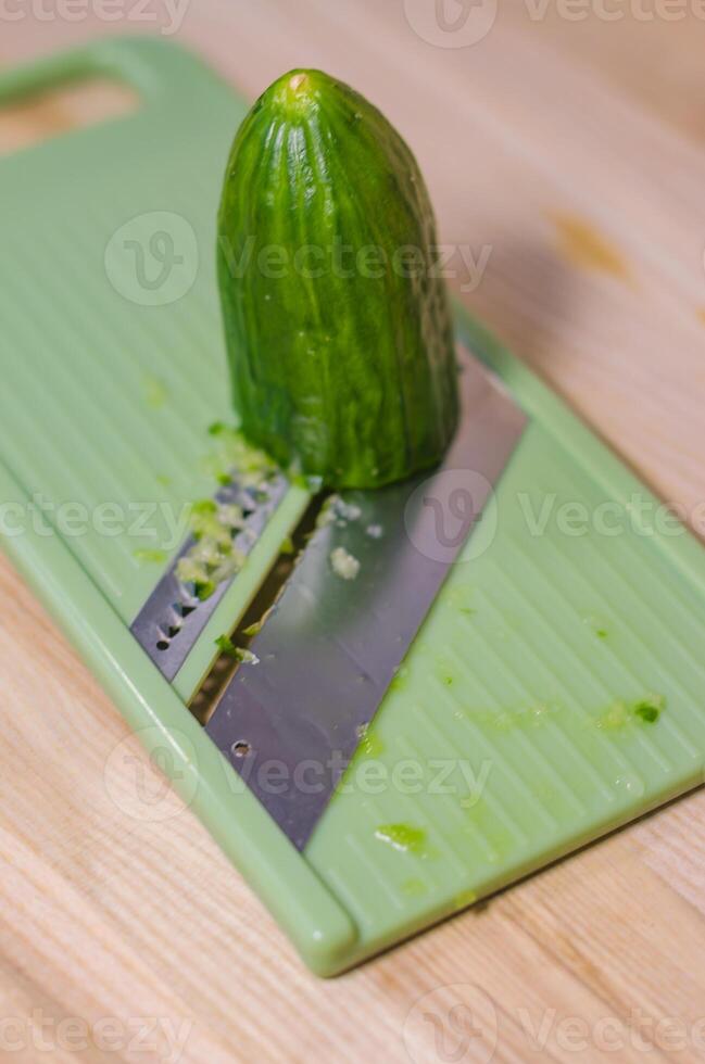 Fresh green cucumber on a light green mandoline slicer, ready for slicing . High quality photo