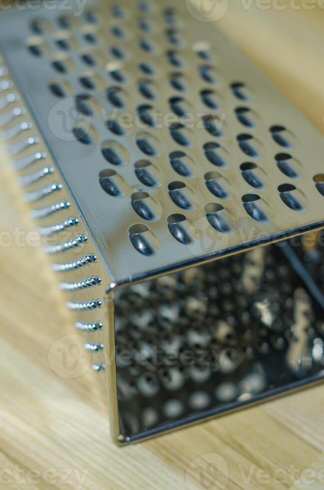 Stainless steel box-shaped four-sided kitchen grater lies wooden cutting board . High quality photo