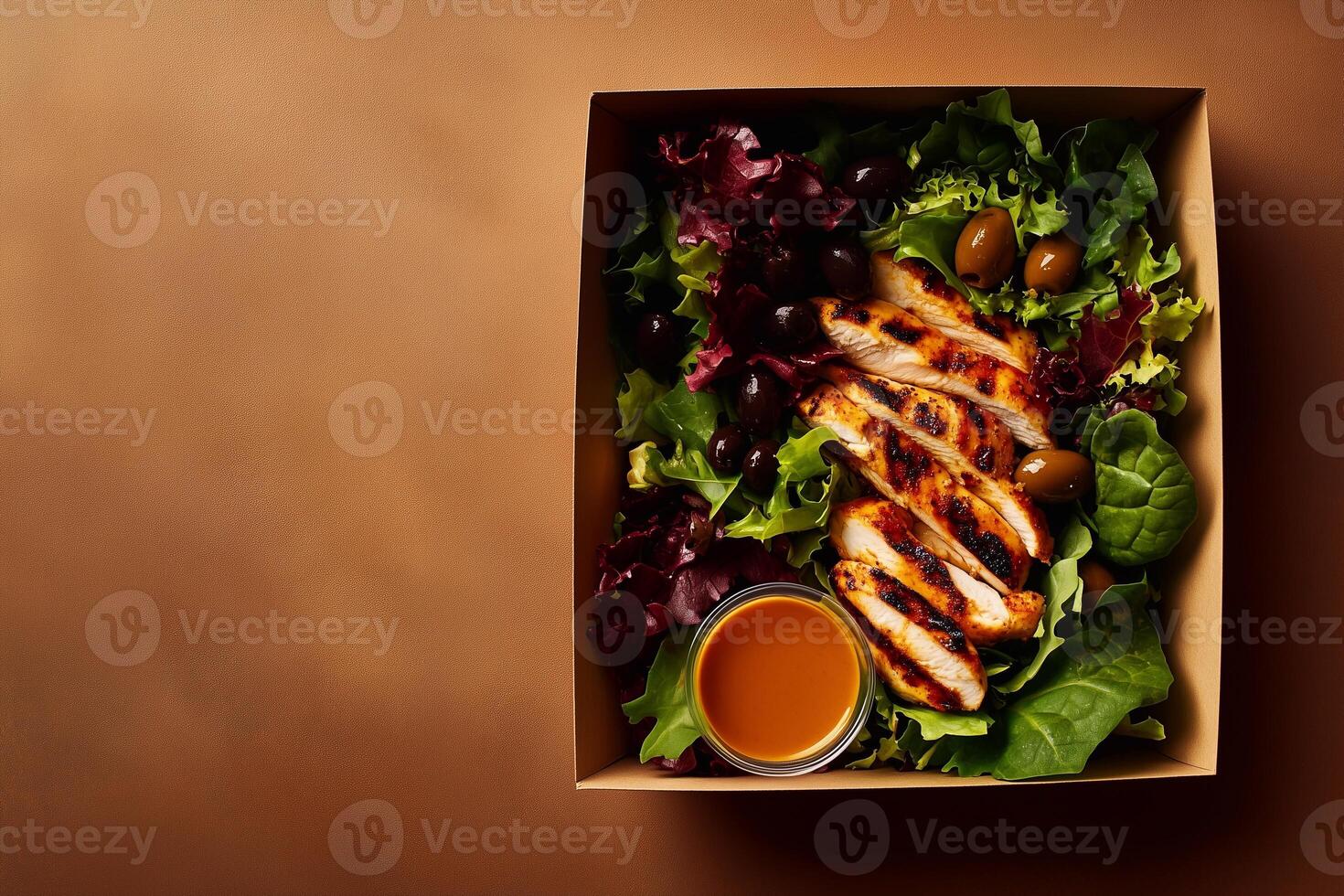 A grab-and-go salad in a cardboard box with grilled chicken, fresh lettuce, black and green olives, and a side of rich dressing, set on a warm brown background. . photo