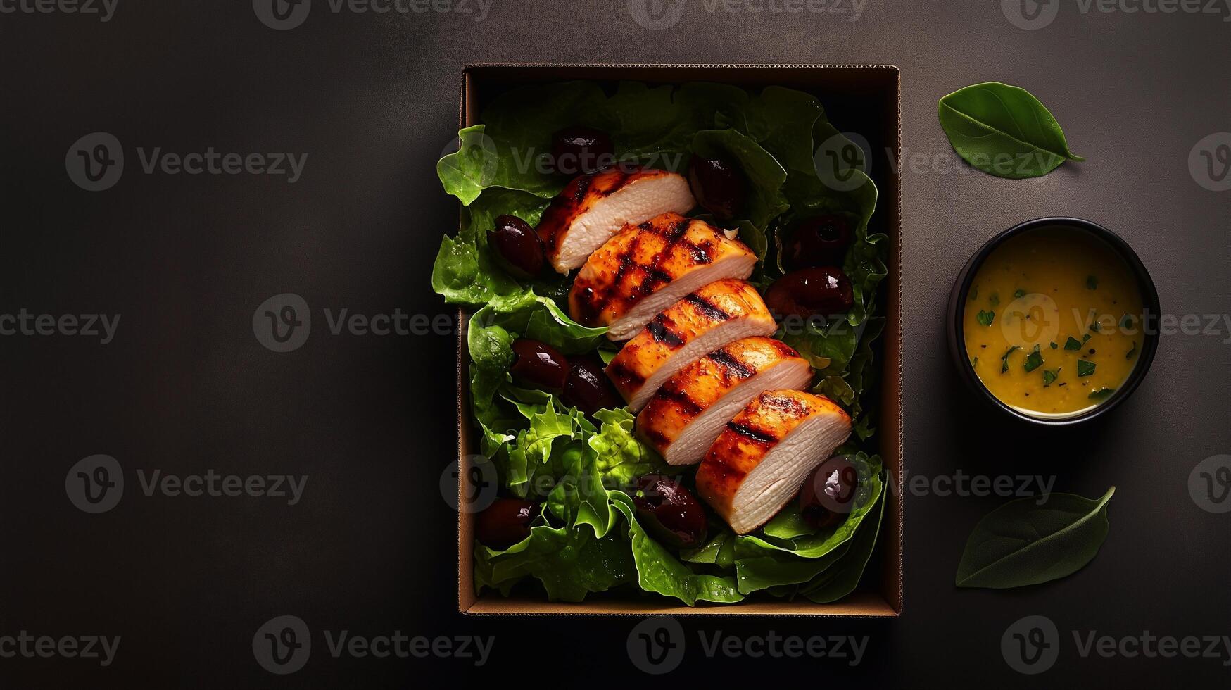 A neatly arranged grab-and-go salad in a rustic cardboard box with grilled chicken, fresh lettuce, black olives, and a side of lemon dressing, set on a dark background. . photo