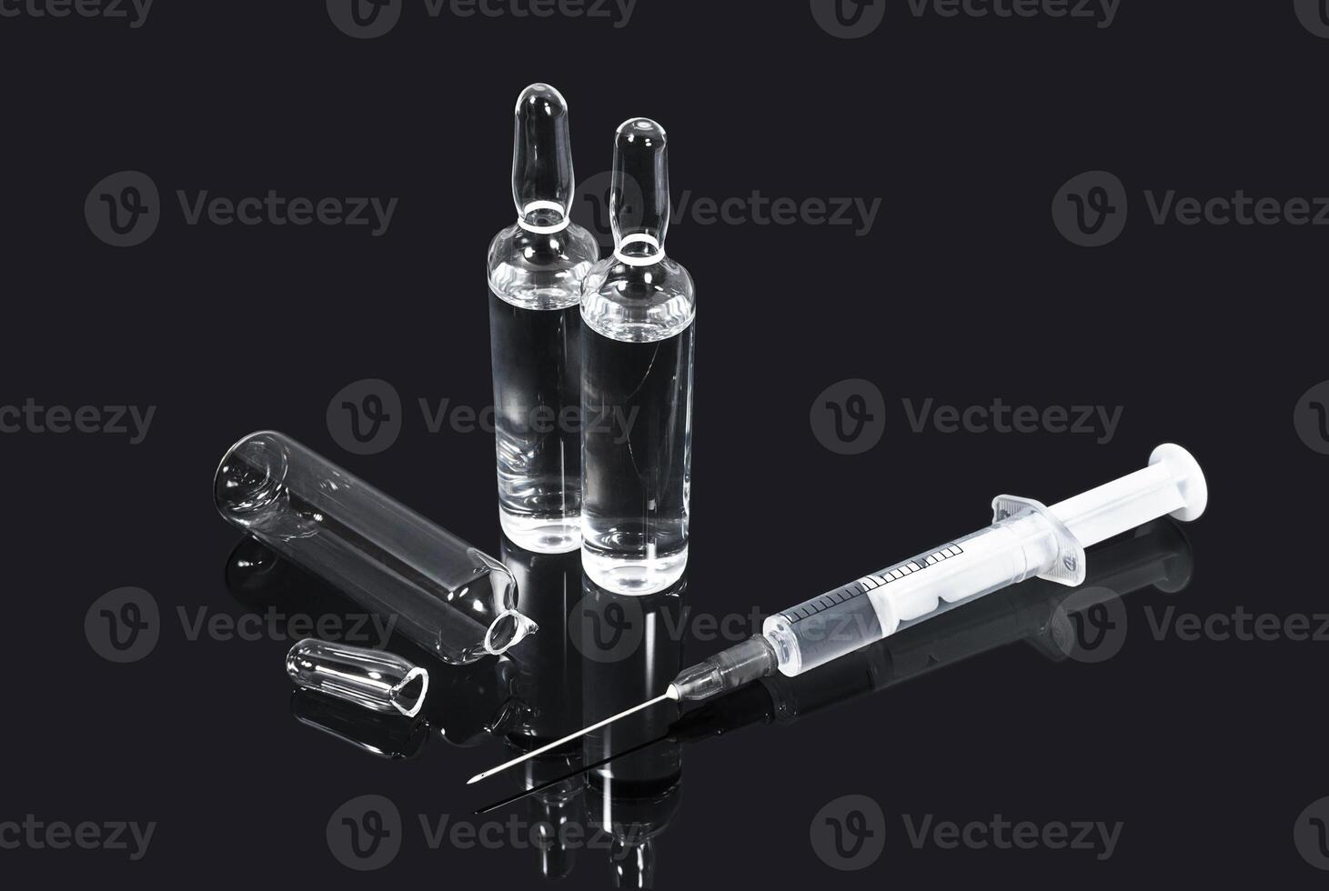 Ampoules with transparent vaccine and syringe on dark background photo