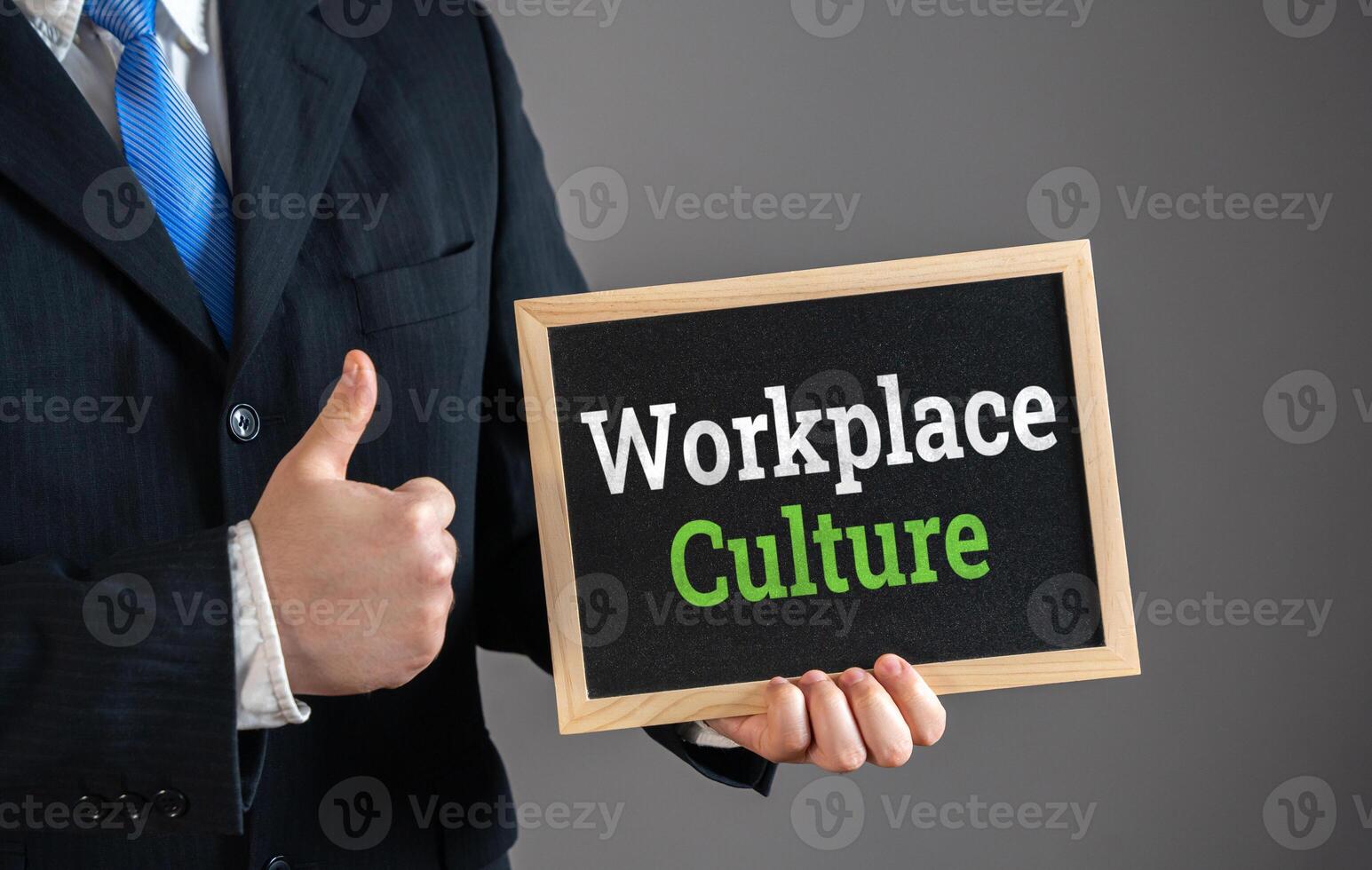 Businessman holding sign with Workplace Culture and giving thumbs up in approval. Positive company environment, teamwork, corporate values, employee engagement. Office morale. photo