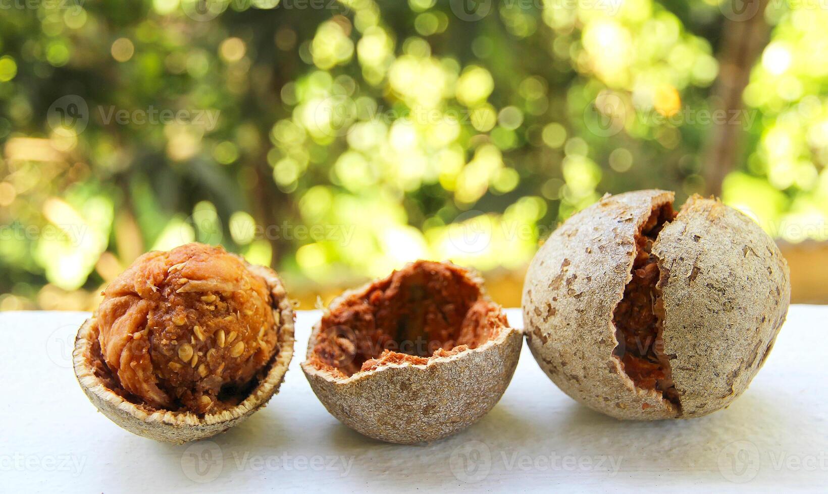 Close up of wood apple whole and cut into two halves - one of the famous fruits of South Asia, on white table and natural green blurred background photo