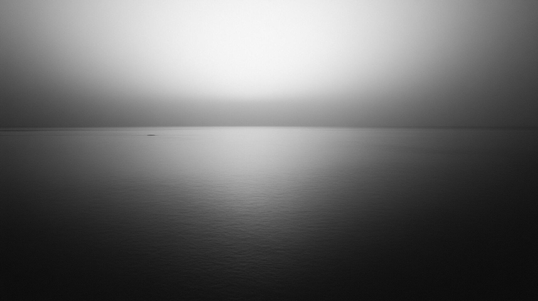 Monochromatic seascape exhibiting stark contrast between luminous sky and calm water, minimal horizon and subtle texture gradients. photo