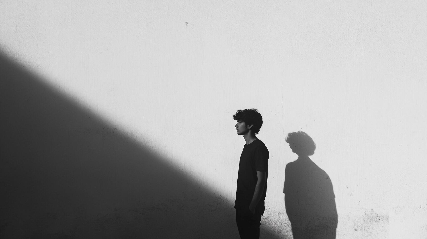 A monochrome portrait features a young man in profile, starkly contrasted against a sunlit wall, casting a shadow. Simple and profound. photo
