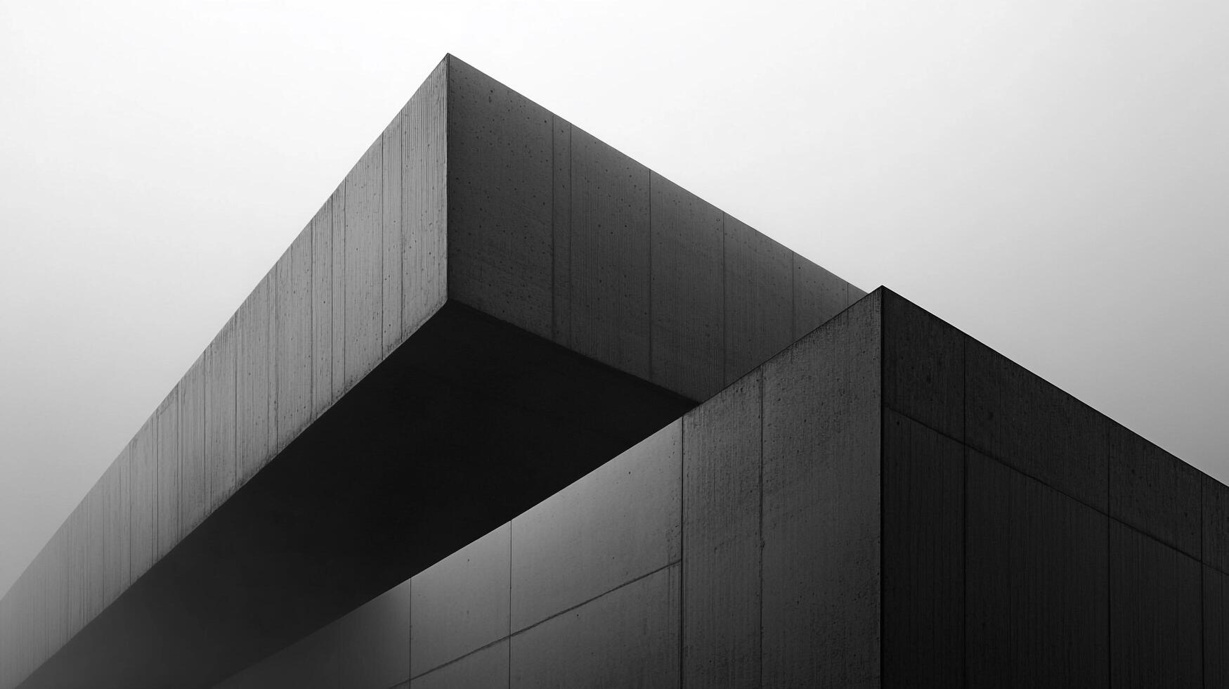 Monochromatic building corner with sharp lines, a modern concrete aesthetic, and structural intersection under a grey sky. Architectural geometry. photo