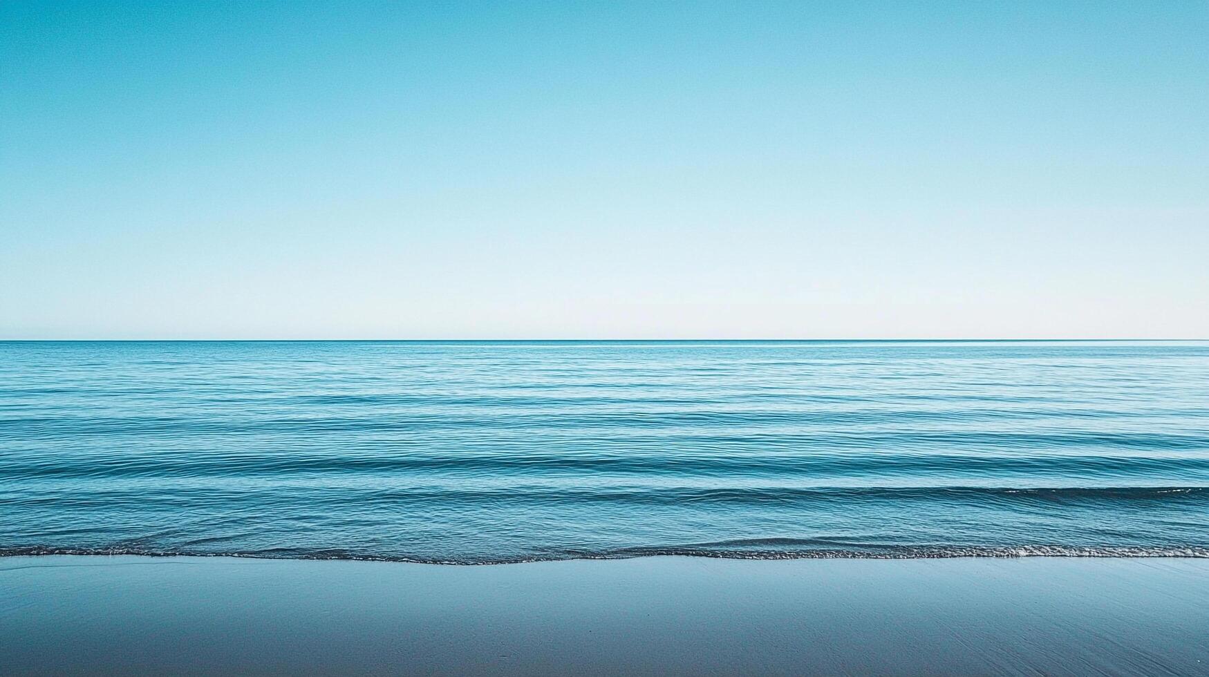 A serene seascape with gentle waves meeting a sandy shore under a clear, tranquil sky in shades of blue. Calm and peaceful horizon. photo