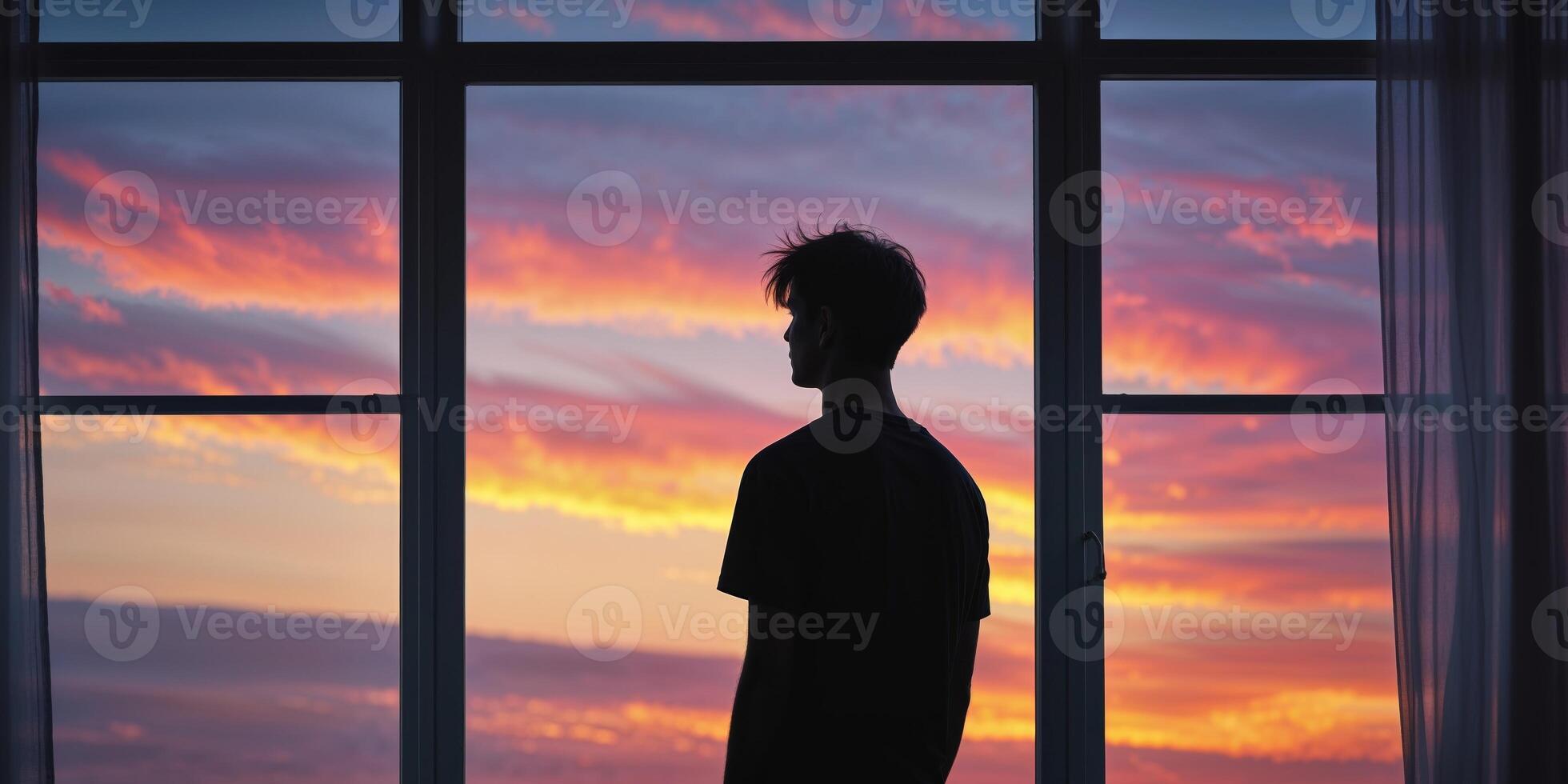Silhouette of a young man looking out the window at the sunset. photo