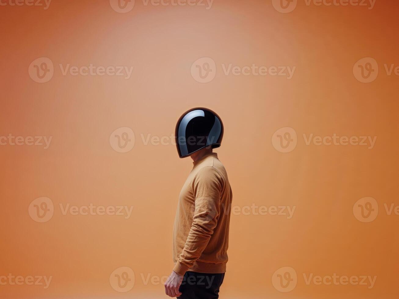 Man in a black helmet stands in front of a bright orange background. photo