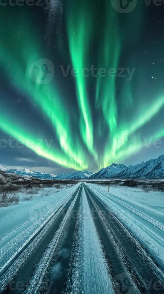 Colorful auroras illuminate a snow-covered road in a remote mountain landscape at night photo