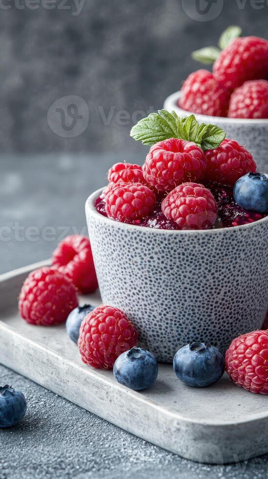 Fresh raspberries and blueberries arranged in a textured bowl with mint leaves on a rustic table photo