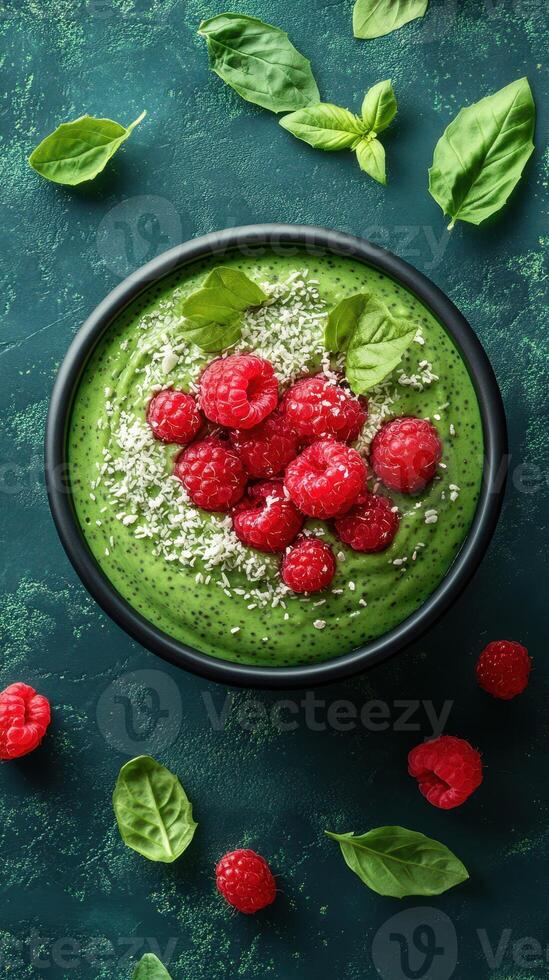 Smoothie bowl topped with fresh raspberries and basil on a textured green background photo