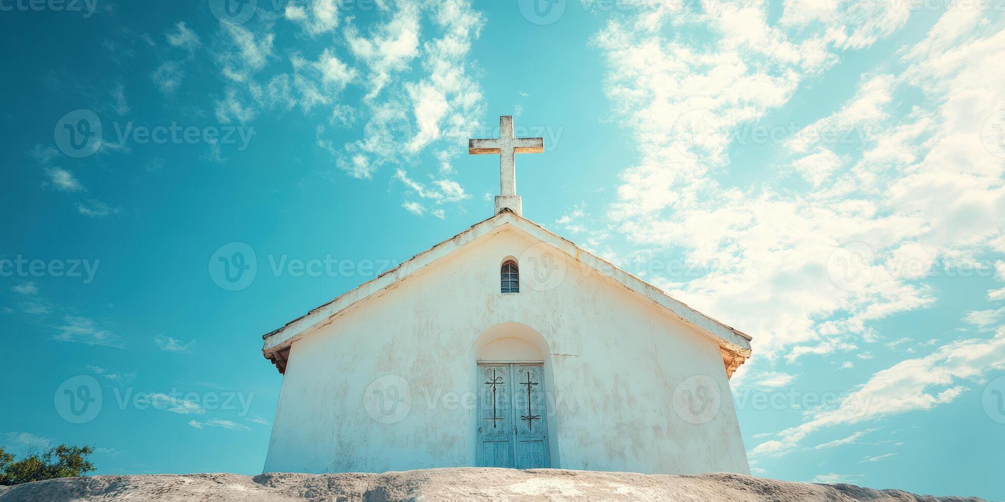 Small white church with cross against a blue sky and clouds on a sunny day in a tranquil setting photo