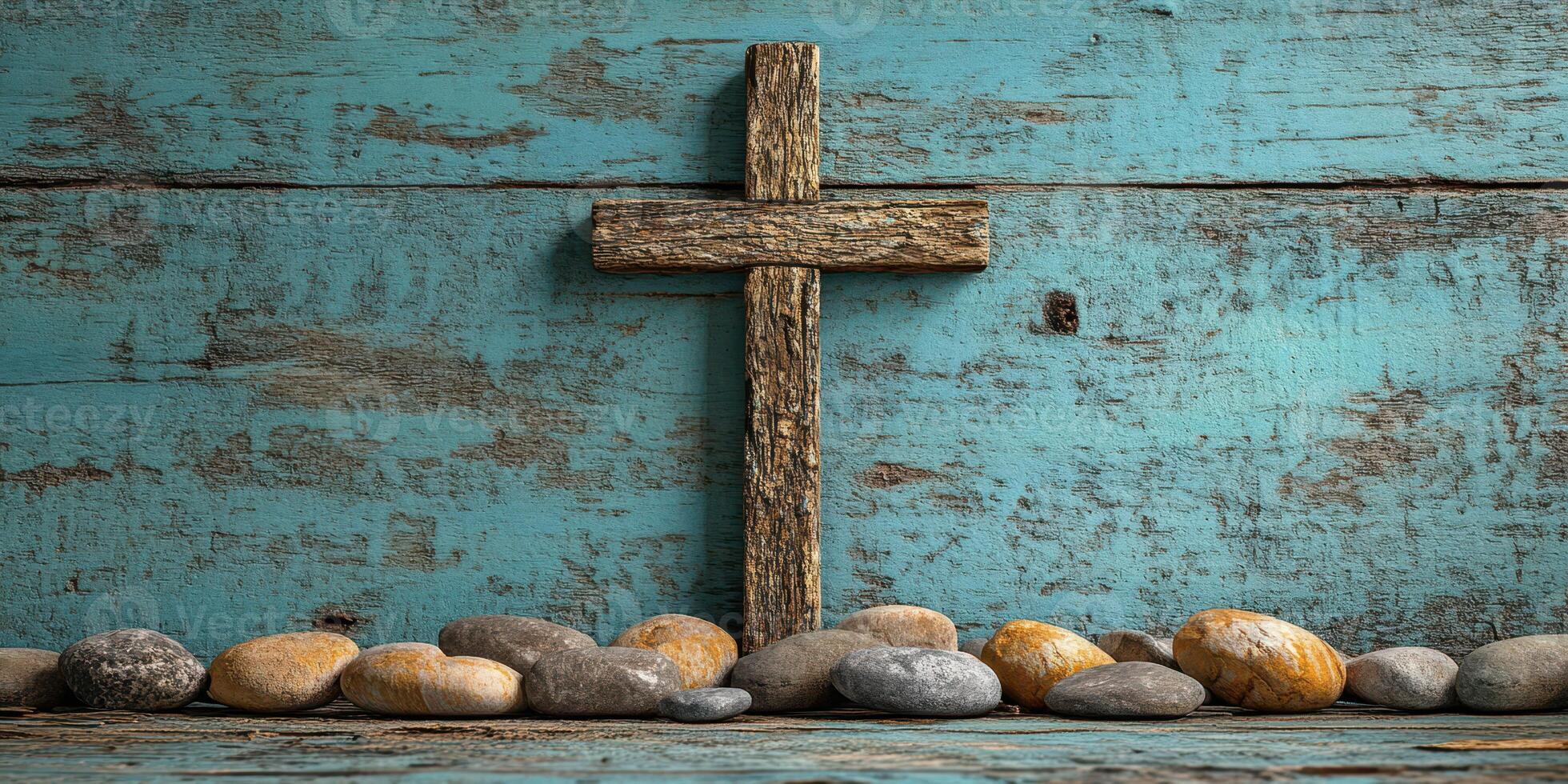 Wooden cross placed on a blue wooden background with smooth pebbles arranged below it photo