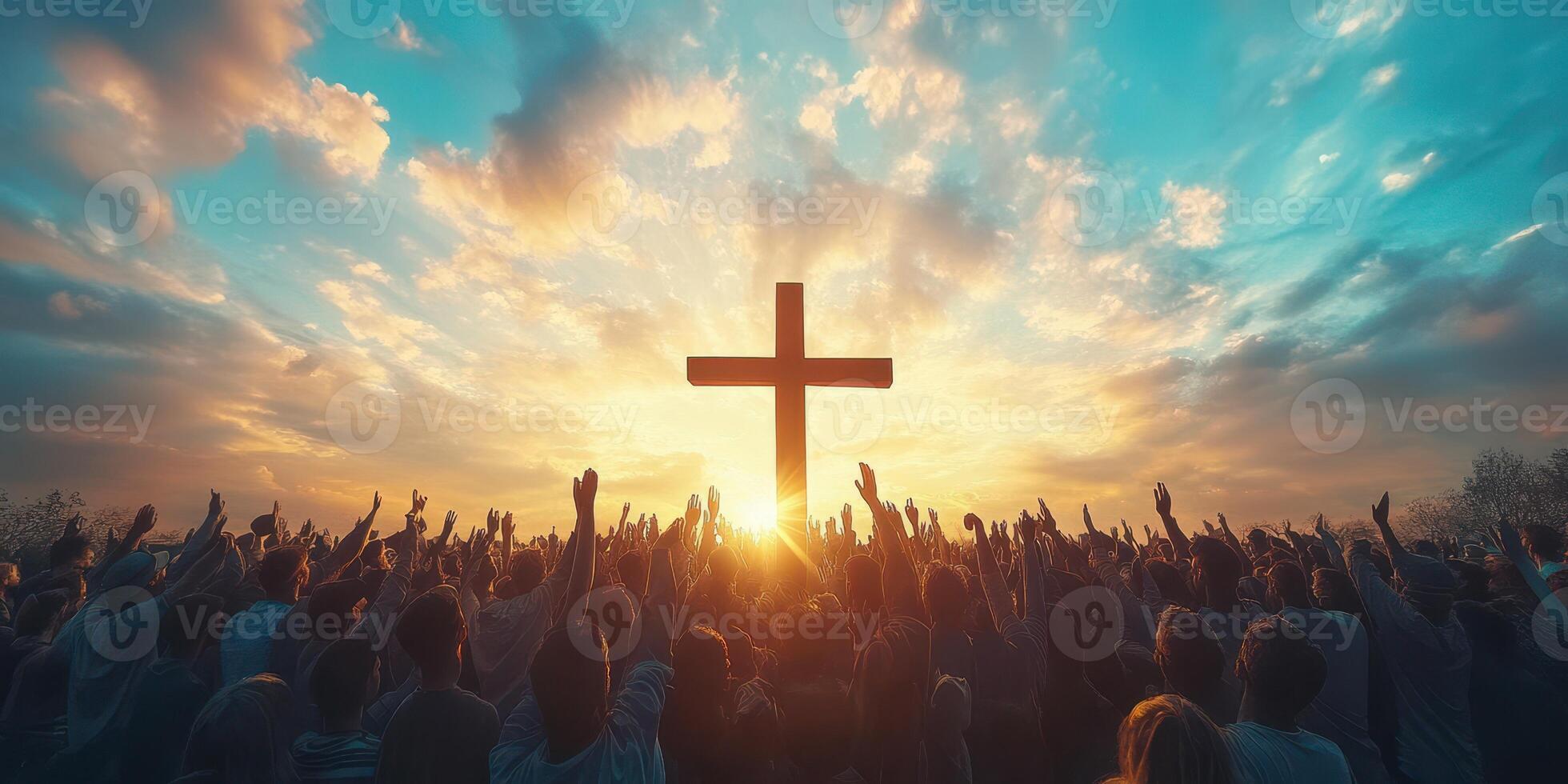 Large crowd raising hands in worship during sunset behind a prominent cross in a serene sky photo