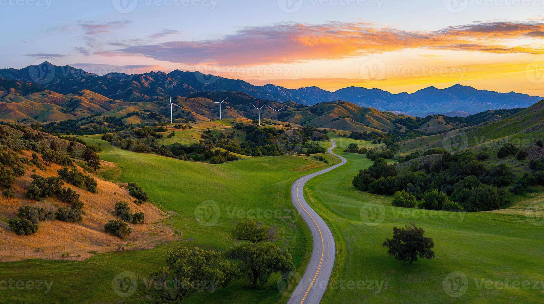 Scenic Winding Road Through Lush Green Valley at Sunset with Wind Turbines and Mountains photo