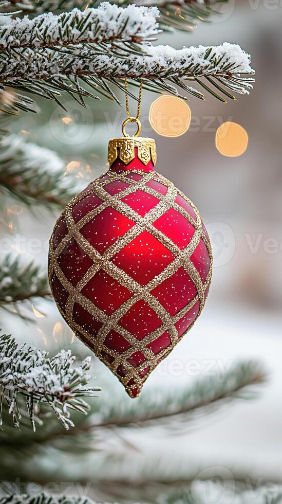 Red christmas ornament with gold accents hanging on a snowy evergreen tree photo