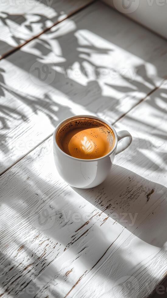 Cup of coffee resting on a wooden table with shadows from leaves photo