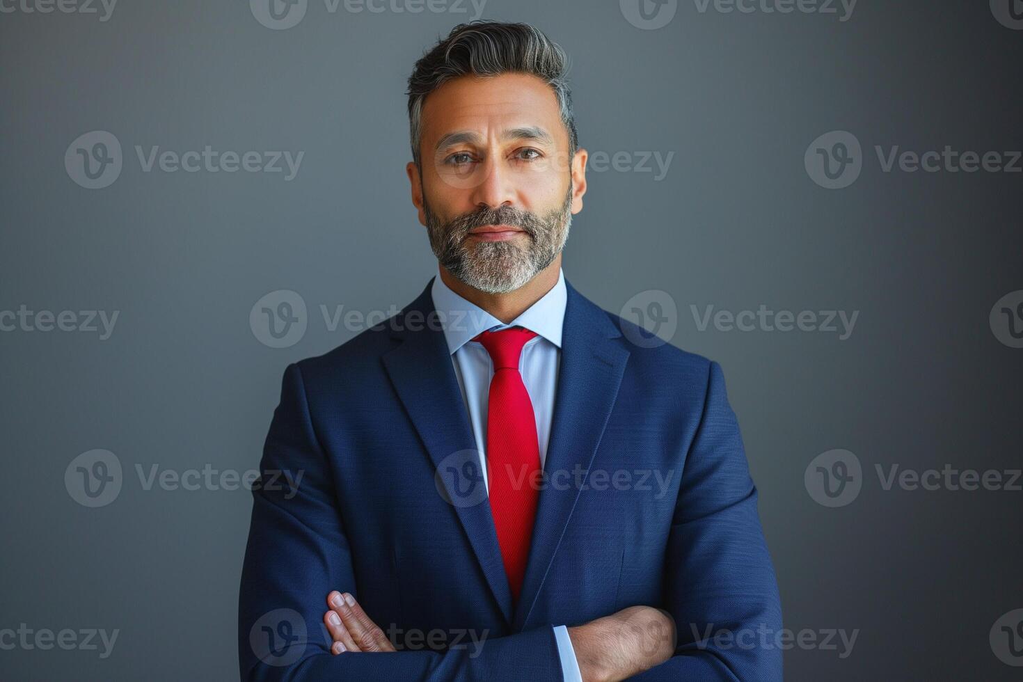 Confident South Asian man in a suit poses with arms crossed, exuding professionalism against a neutral background. photo