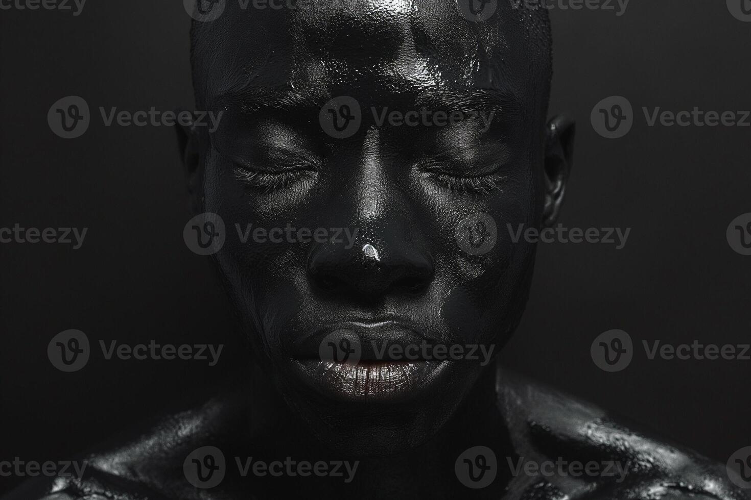 A serene male model with deep black face paint, eyes closed, evoking a strong emotional connection against a dark background. photo