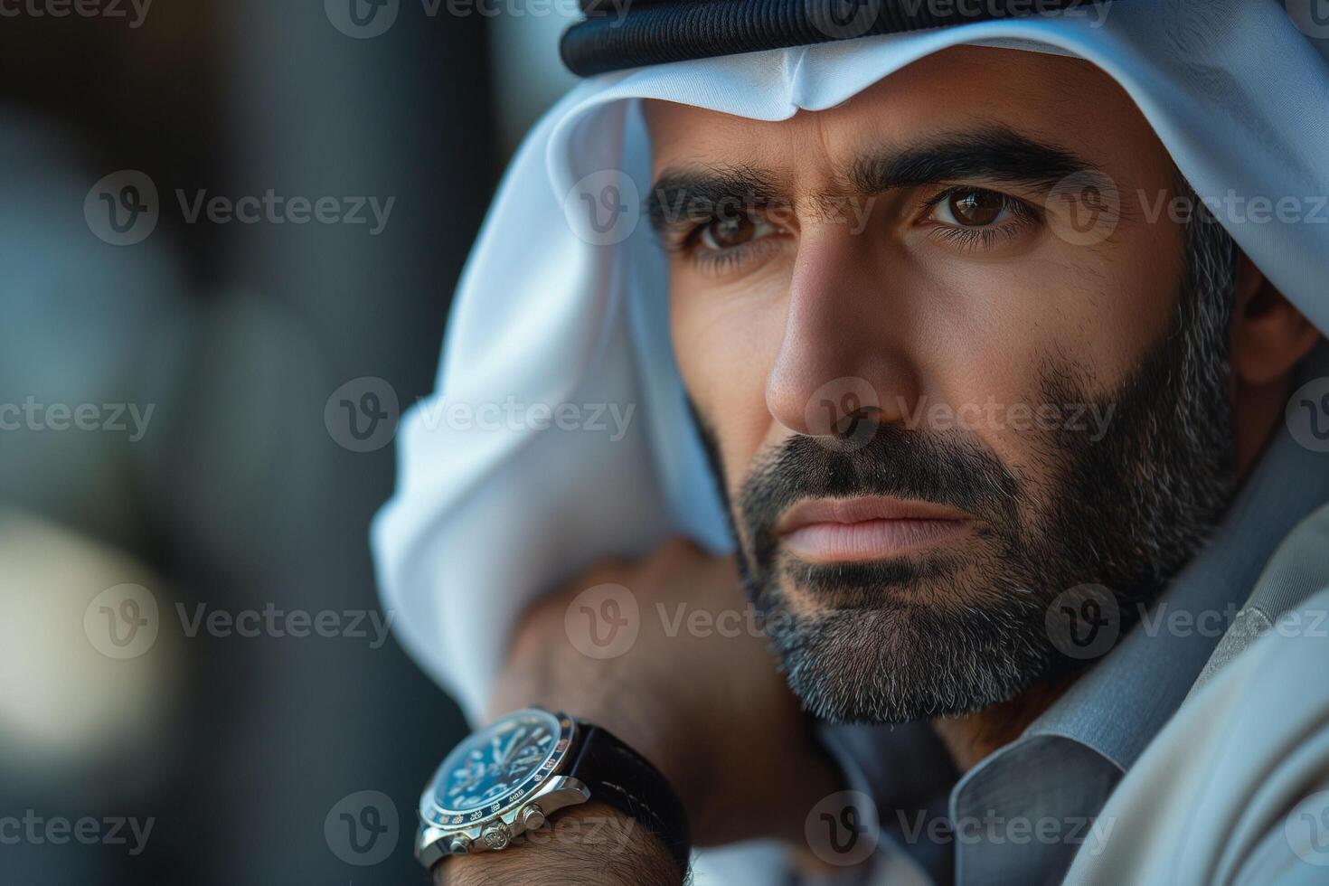 A focused Middle-Eastern man in traditional attire gazes thoughtfully, showcasing his beard and stylish watch. photo