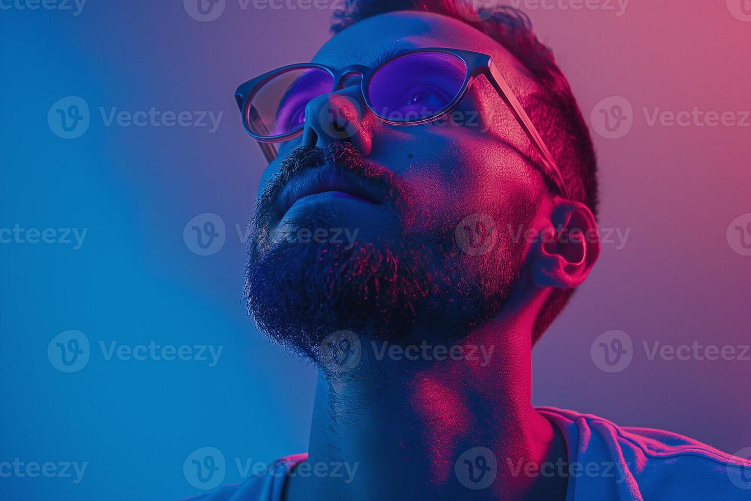 A young Hispanic man gazes upward, illuminated in striking pink and blue hues, showcasing a thoughtful expression. photo