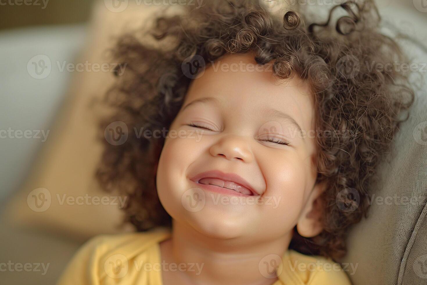 A cheerful mixed-race girl with curly hair smiles brightly, radiating joy and innocence in a cozy setting. photo