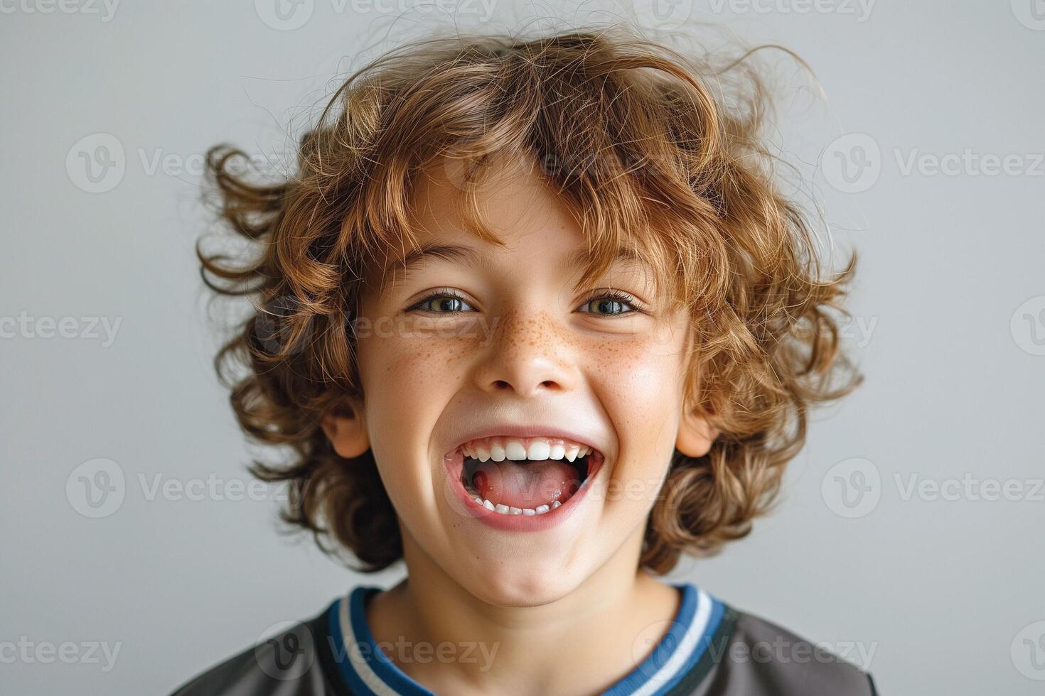 A joyful young Caucasian boy with curly hair and freckles smiles broadly against a light background. photo