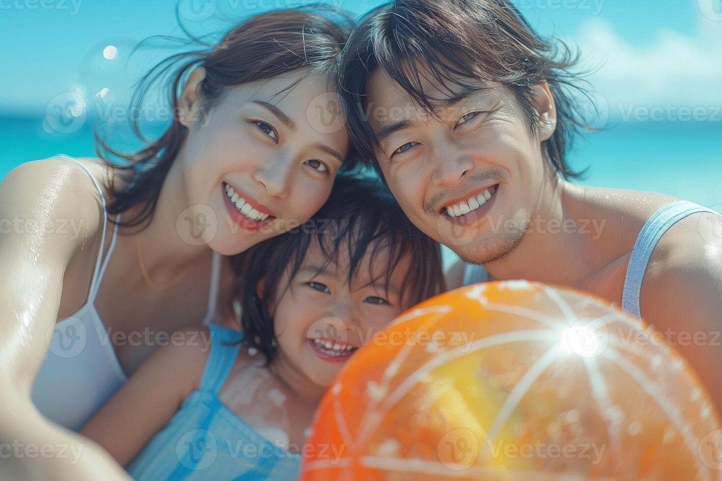 A joyful family of three, a young Asian couple and their daughter, enjoying a sunny beach day with a bright orange beach ball. photo