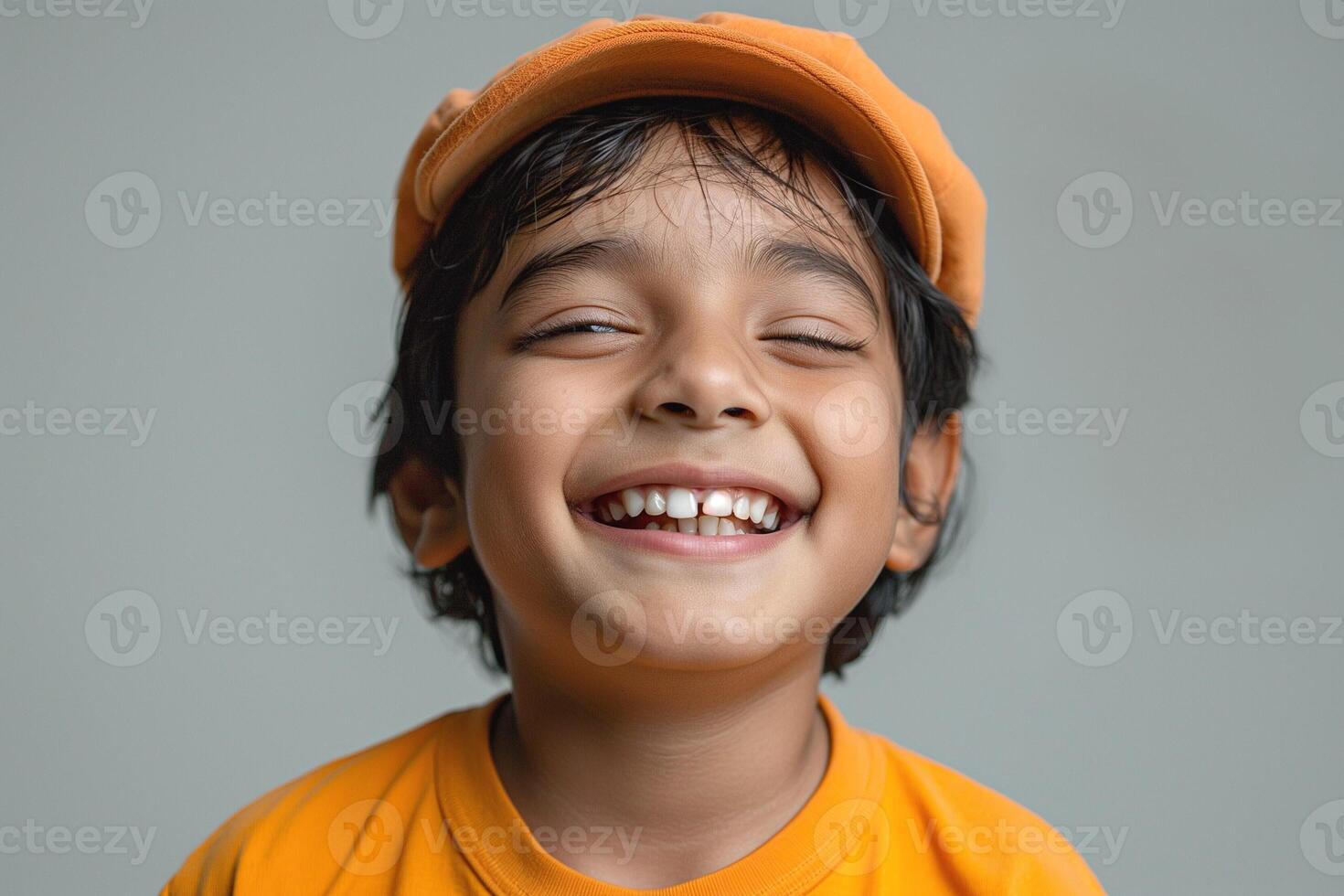 Joyful young boy with dark hair and a bright orange hat, smiling widely and radiating happiness against a simple background. photo
