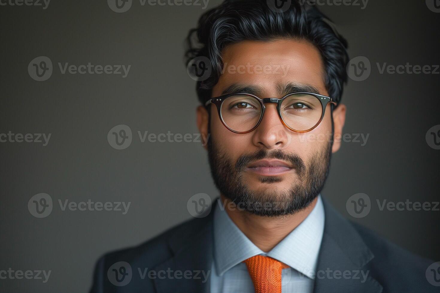 Confident South Asian businessman with glasses in a dark suit and vibrant orange tie, exuding professionalism and charisma. photo