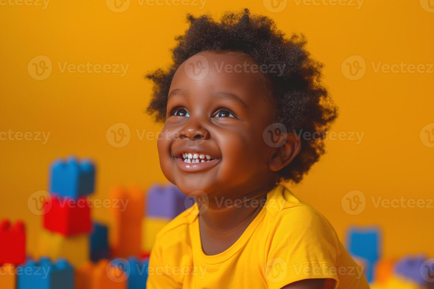 A joyful Black boy with curly hair smiles brightly against a vibrant yellow background, surrounded by colorful building blocks. photo