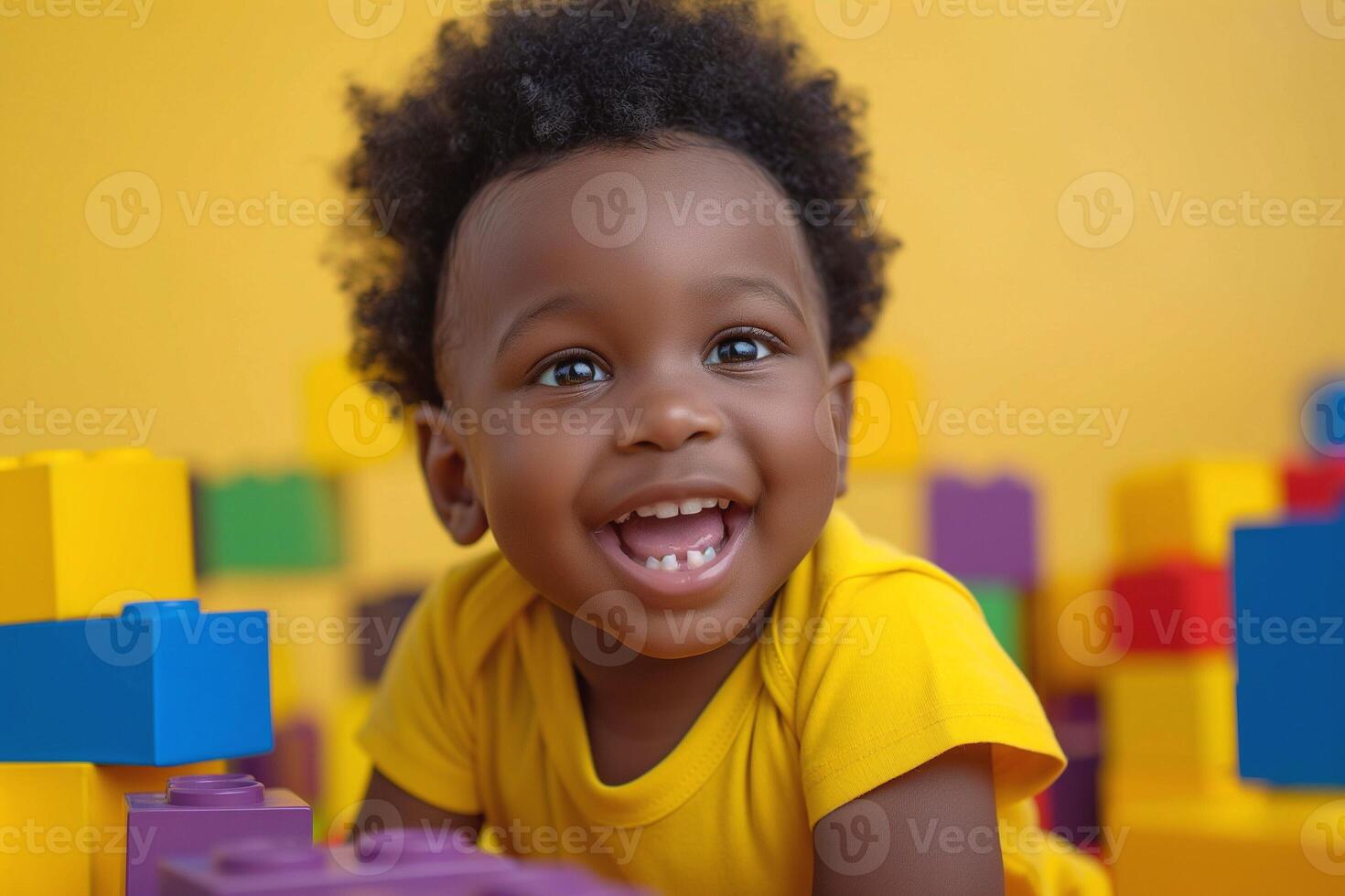 A joyful Black toddler smiles brightly while playing with colorful building blocks in a sunny yellow setting. photo