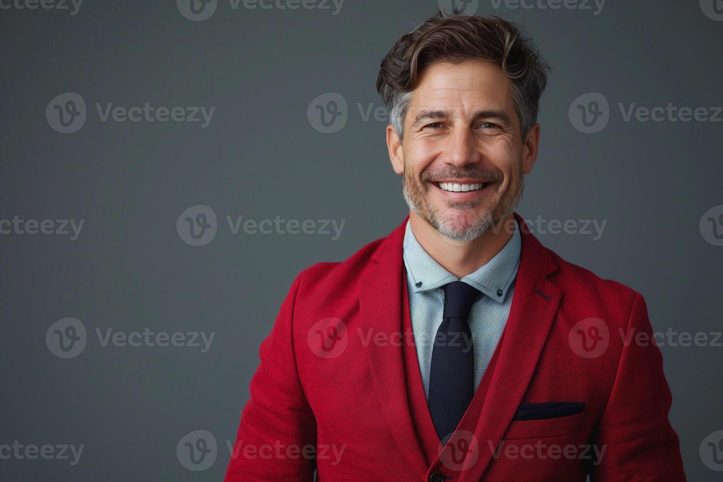 A smiling middle-aged Caucasian man in a red blazer and tie poses confidently against a gray background. photo