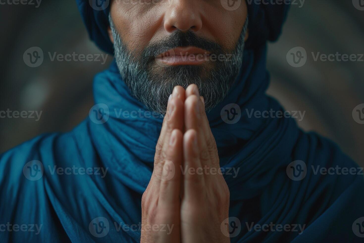 A Middle-Eastern man in traditional attire, with a thoughtful expression, prays with clasped hands against an artistic backdrop. photo