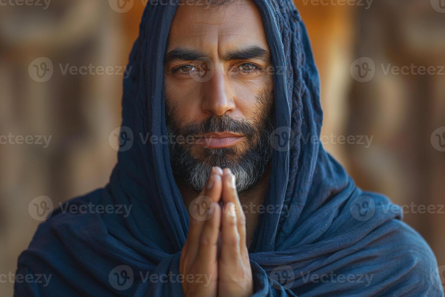 A Middle-Eastern man with a beard, dressed in a dark shawl, gazes intently while his hands are in a prayer position. photo