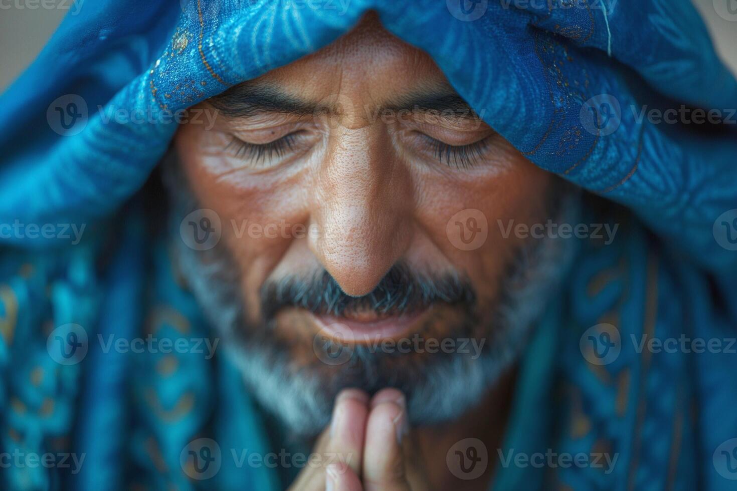 A contemplative Middle-Eastern man in a blue shawl, with clasped hands, embodying peace and spirituality. photo
