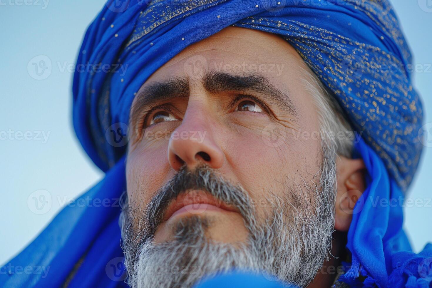 A contemplative Middle-Eastern man with a blue turban gazes thoughtfully into the distance. photo