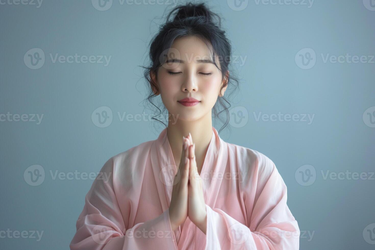 A serene young Asian woman practices mindfulness in a soft pink robe, emphasizing peace and tranquility with her eyes closed. photo