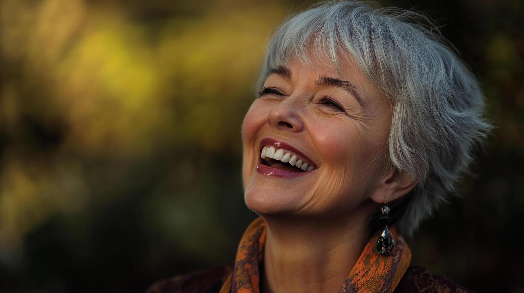 Radiant joy illuminates a woman's face as she laughs, her eyes closed and head tilted back against a softly blurred nature backdrop. photo