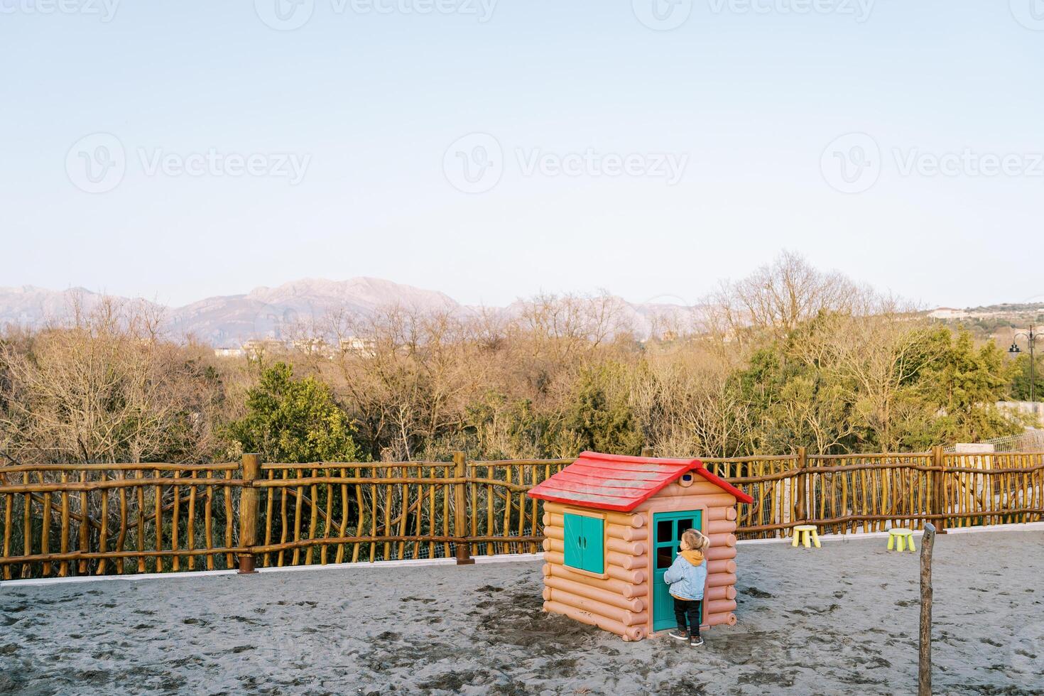 Little girl stands in front of the door of a toy house in the playground photo