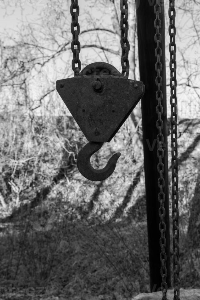 Metal hook and pulley system hanging from a structure in an outdoor area surrounded by trees during daylight hours photo