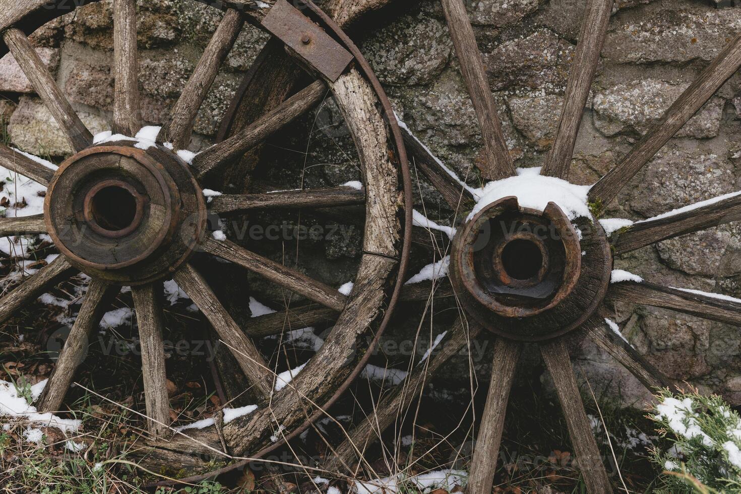 Old wooden wagon wheels resting against a stone wall in the snow during winter photo