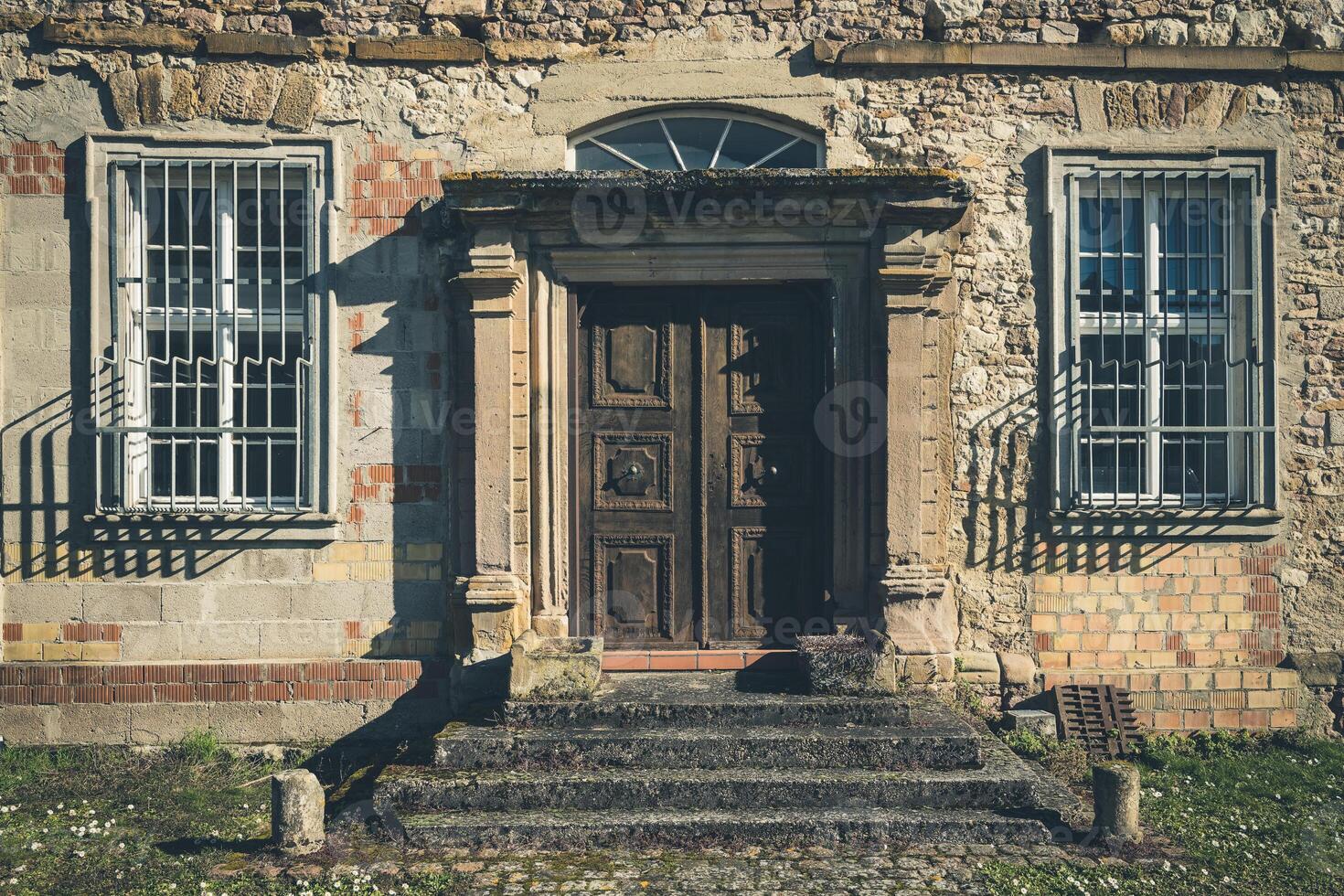 Abandoned building with weathered door and barred windows in a rural setting during daylight photo