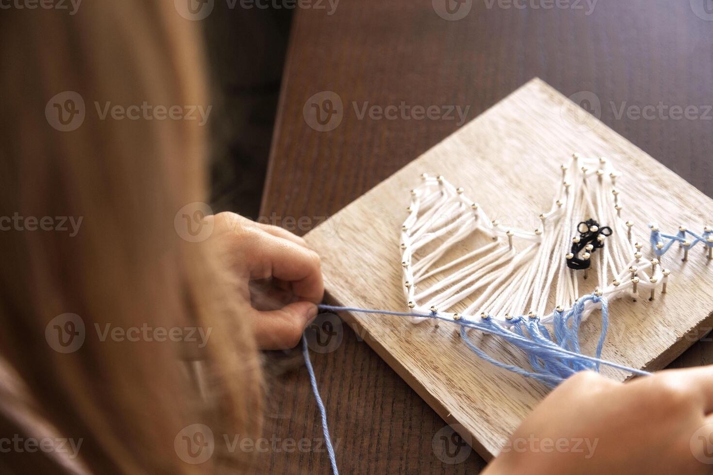 Child weaving string art on wood. Developing patience, creativity, and fine motor skills through crafting photo
