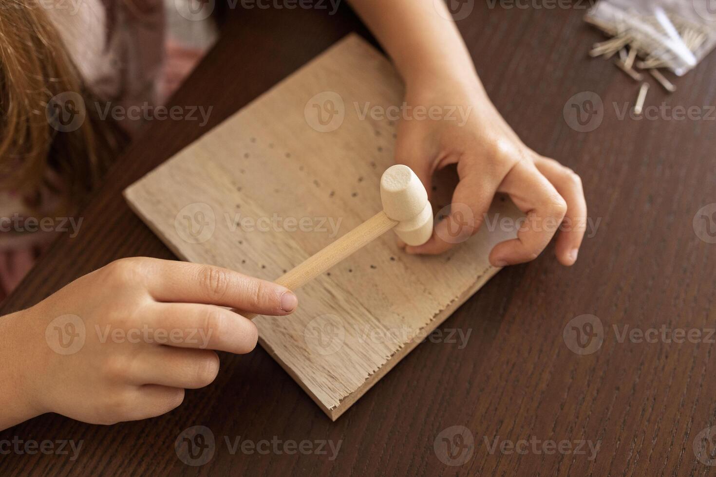 Close-up of a child hands using hammer on wood. Crafting, learning, and building patience. photo