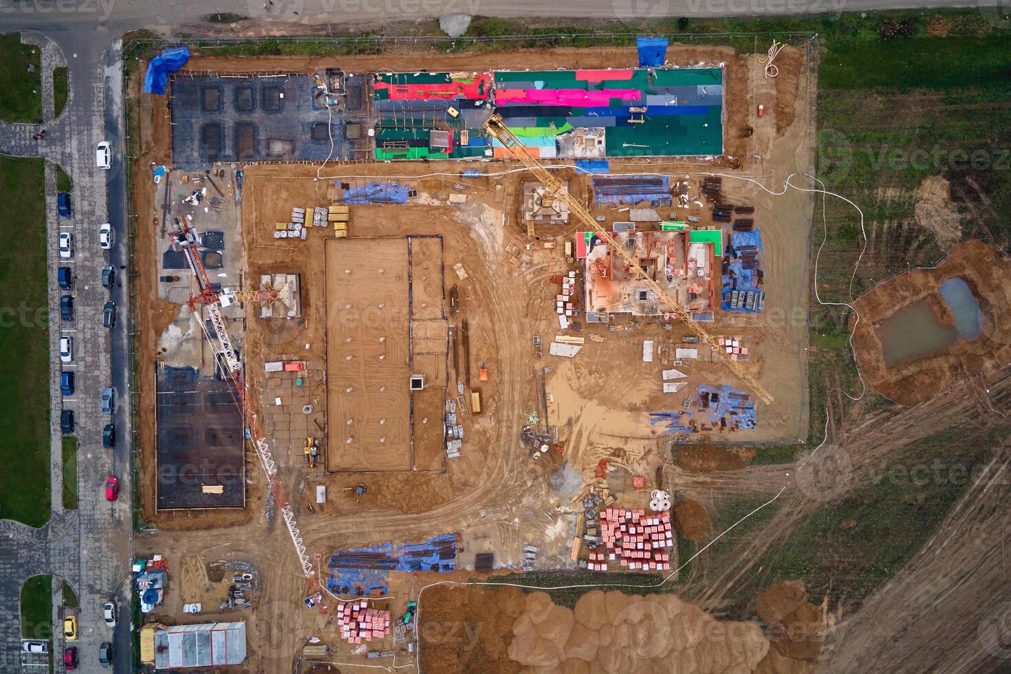 Aerial view of construction site with cranes, foundations and building materials. Residential building under construction. Progress of new development in small town photo